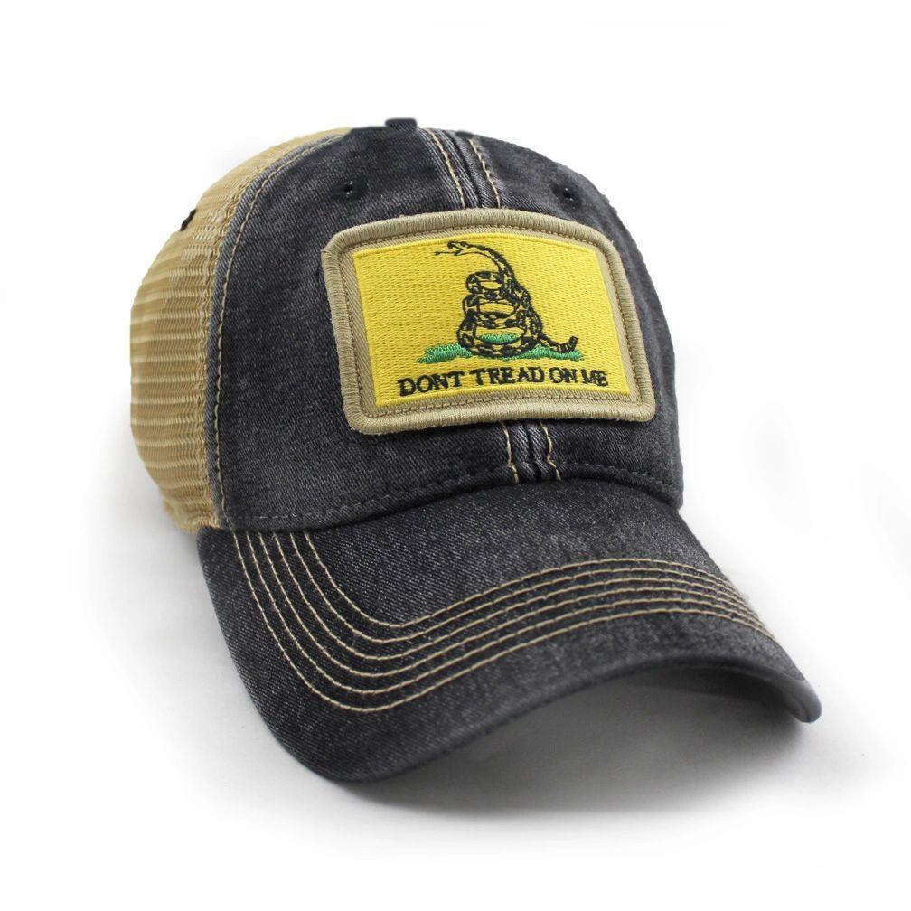 Black trucker hat with khaki mesh back panels and tan stitching laying. Ballcap is embroidered with a patch of the Gadsden flag, the patch has a yellow background with a snake coiled in grass and the words Don't Tread On Me