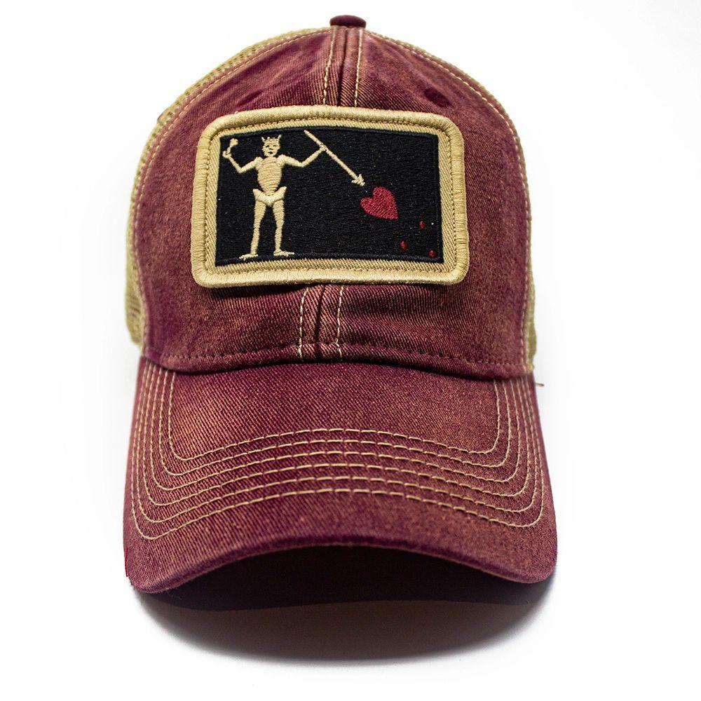 Brick red trucker hat with embroidered Blackbeard pirate flag patch on the center and khaki mesh back panels. Patch depicts a natural colored skeleton with horns piercing a red bleeding heart with a spear. 