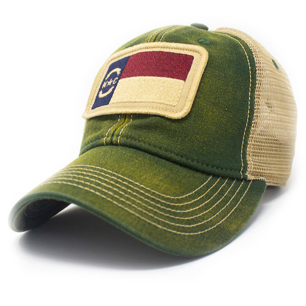 Trucker hat with khaki colored mesh backing, forest green cotton front panel and bill with tan stitching. Ballcap has an embroidered patch of the North Carolina flag in in the center. 