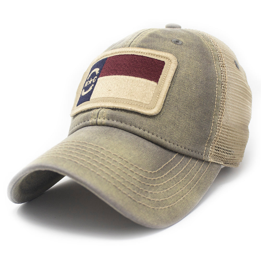 Trucker hat with khaki colored mesh backing, grey cotton front panel and bill with tan stitching. Ballcap has an embroidered patch of the North Carolina flag in in the center.